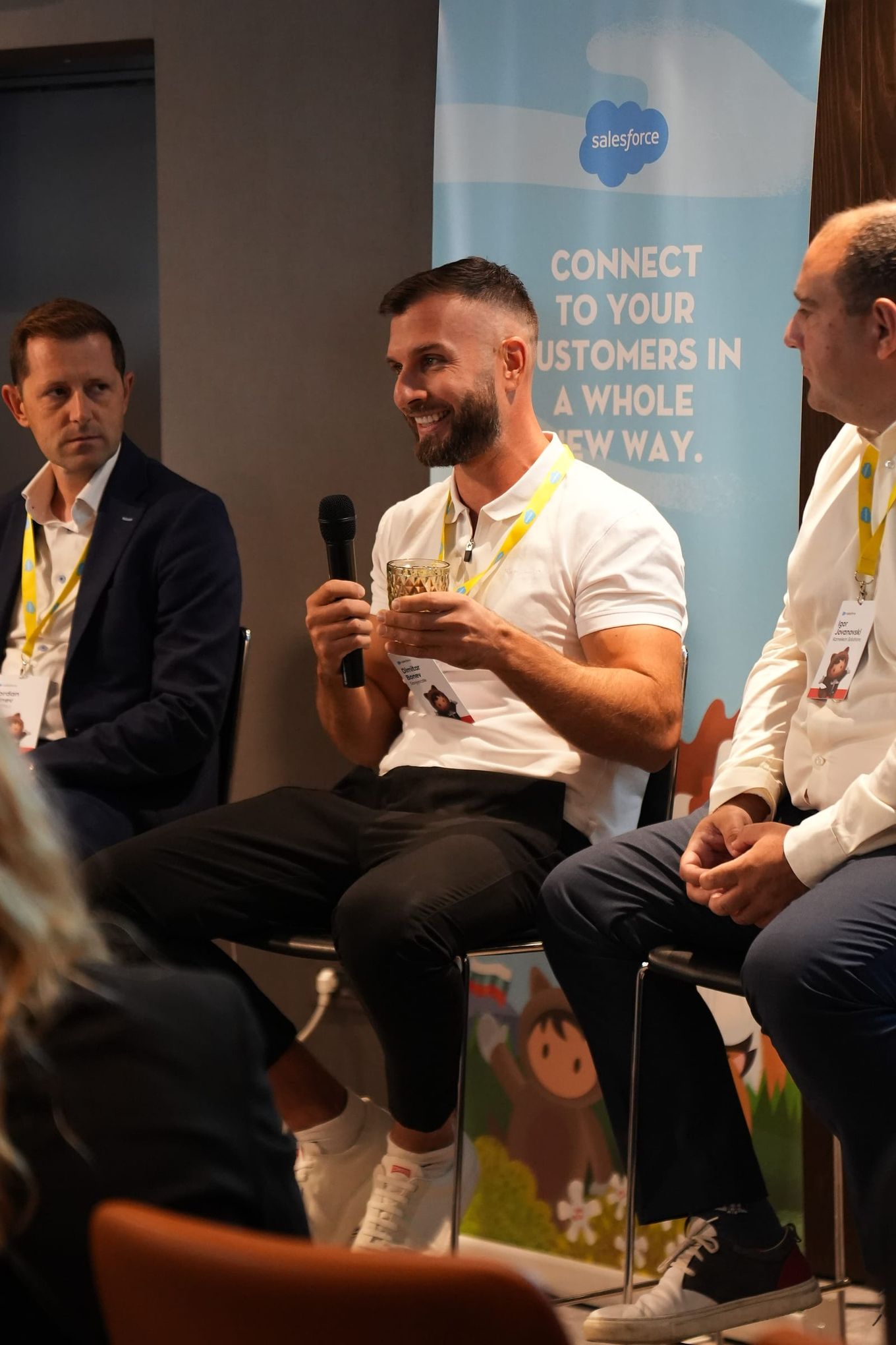 Dimitar Bonev holding a microphone, seated between two other panelists in front of a Salesforce banner.